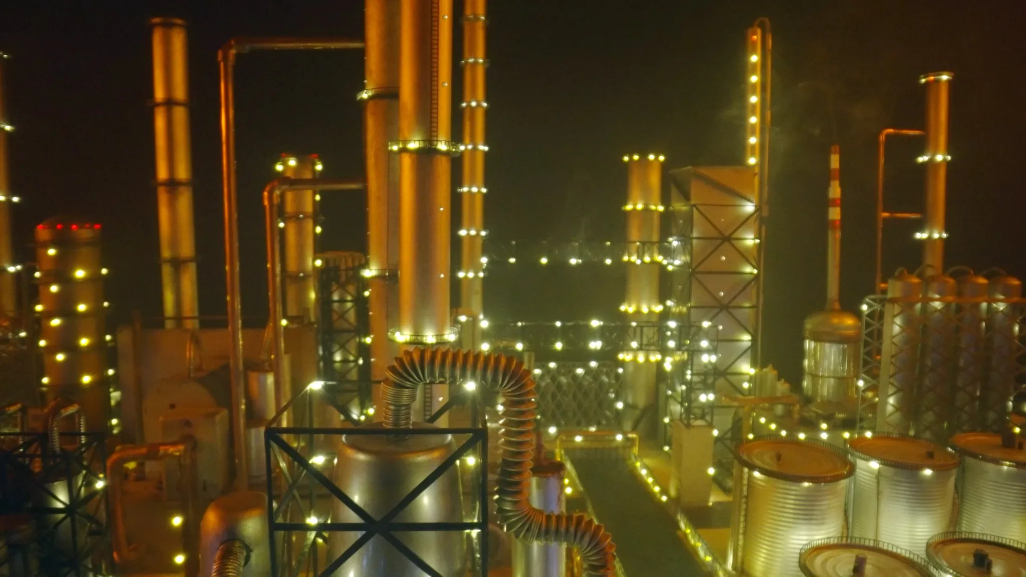 Een olieraffinaderij-industriegebied dat 's nachts verlicht is, gehuld in een sfeervolle oranje gloed te midden van een nevelige omgeving.