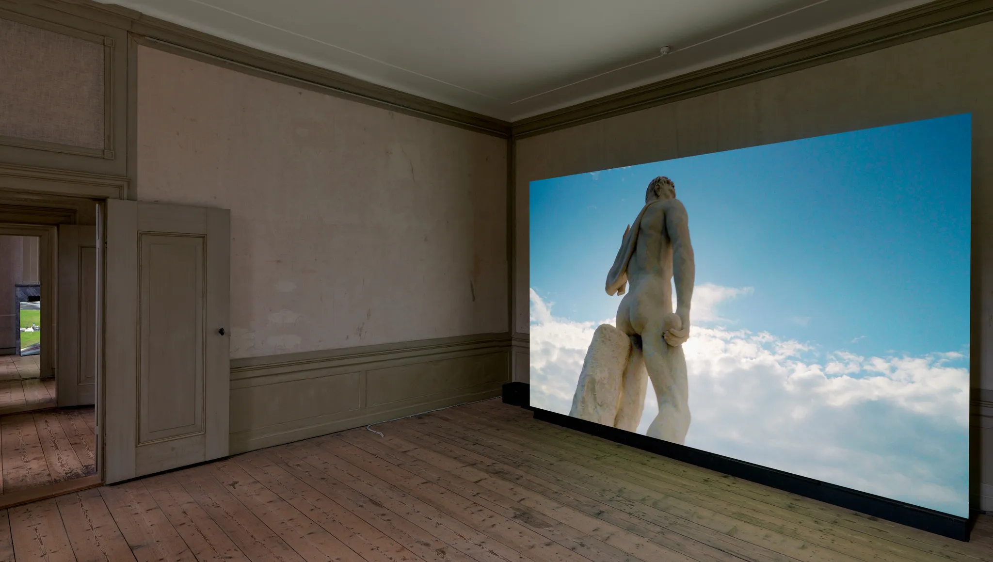 Video op een groot scherm met de achterkant van een hoog klassiek standbeeld van het Stadio dei Marmi voor een blauwe, gedeeltelijk bewolkte lucht.