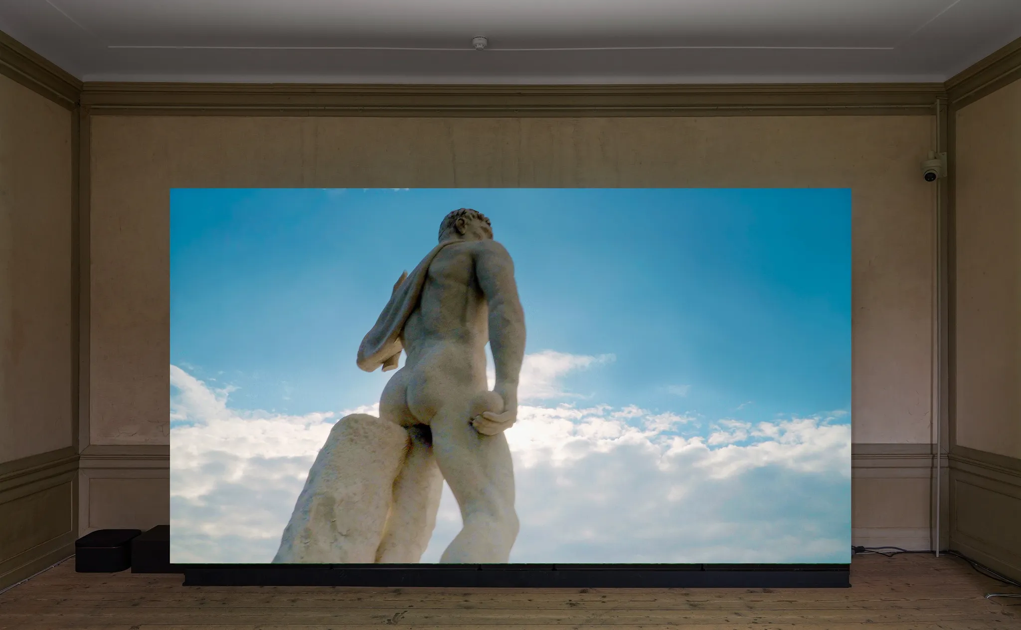 Video op een groot scherm met de achterkant van een hoog klassiek standbeeld van het Stadio dei Marmi voor een blauwe, gedeeltelijk bewolkte lucht.