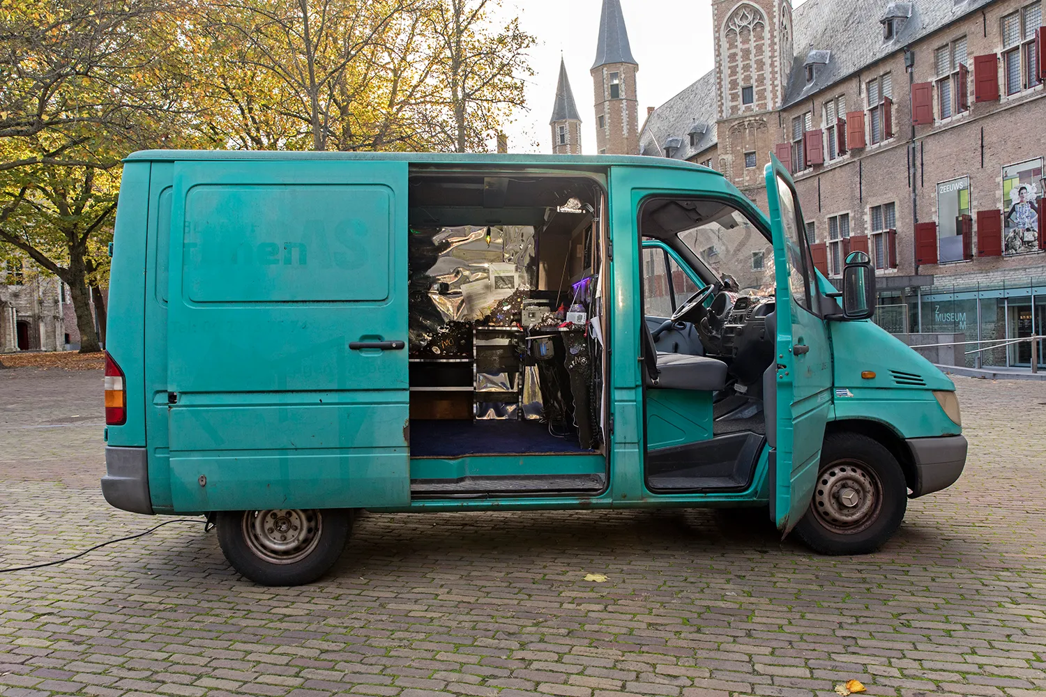 Turquoise busje met deuren open, geparkeerd midden op een plein in Middelburg