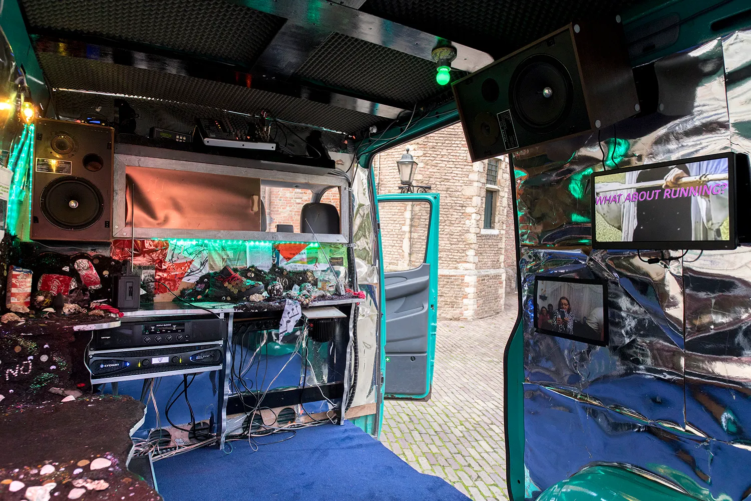 Interieur van het busje met o.a. schermen, luidsprekers, radio's en blauw tapijt