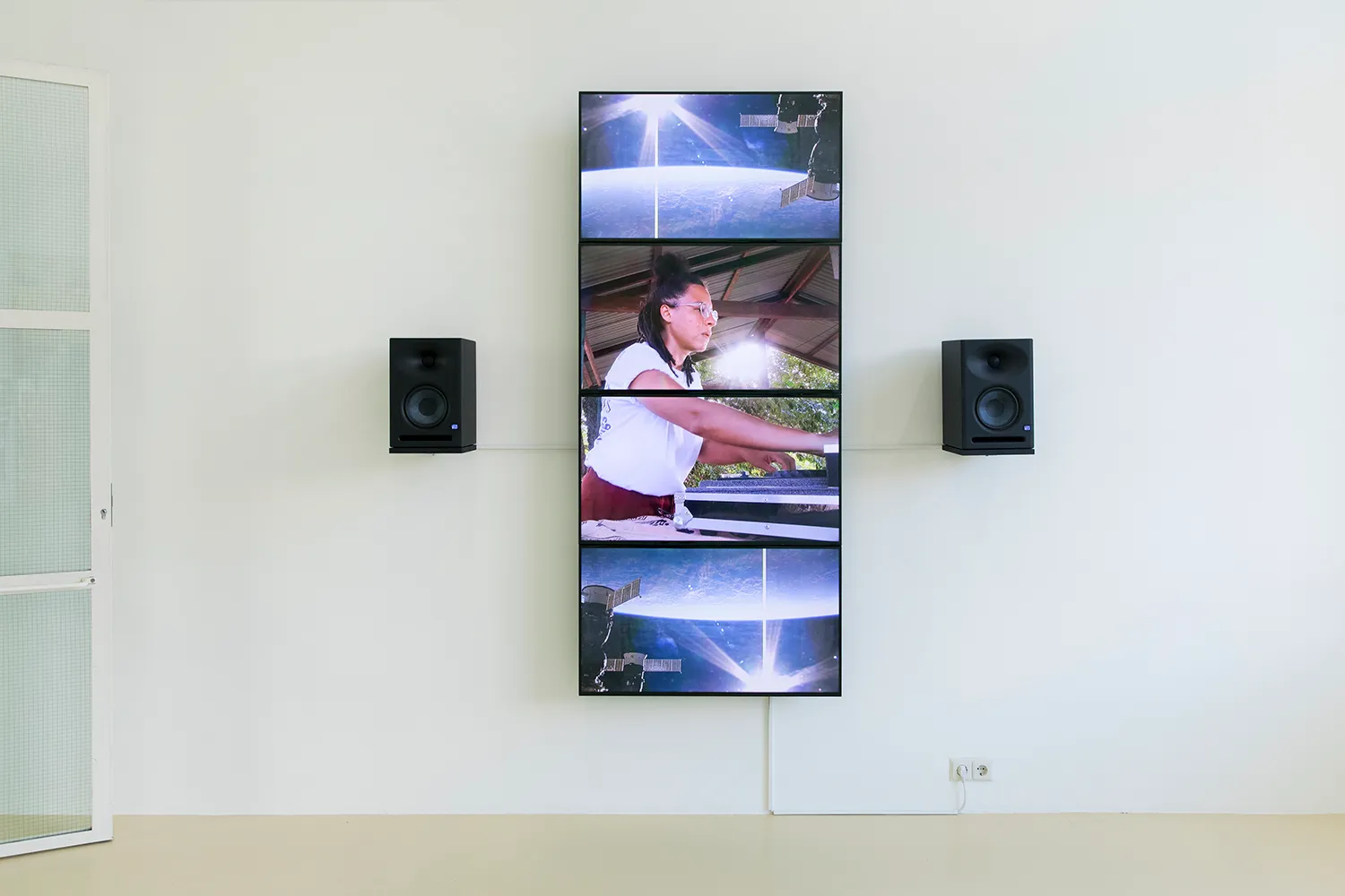4 flatscreens die een verticale streep vormen op de muur met 2 speakers. Een DJ is aan het mixen in het midden van de schermen, omringd door satellietbeelden van een planeet