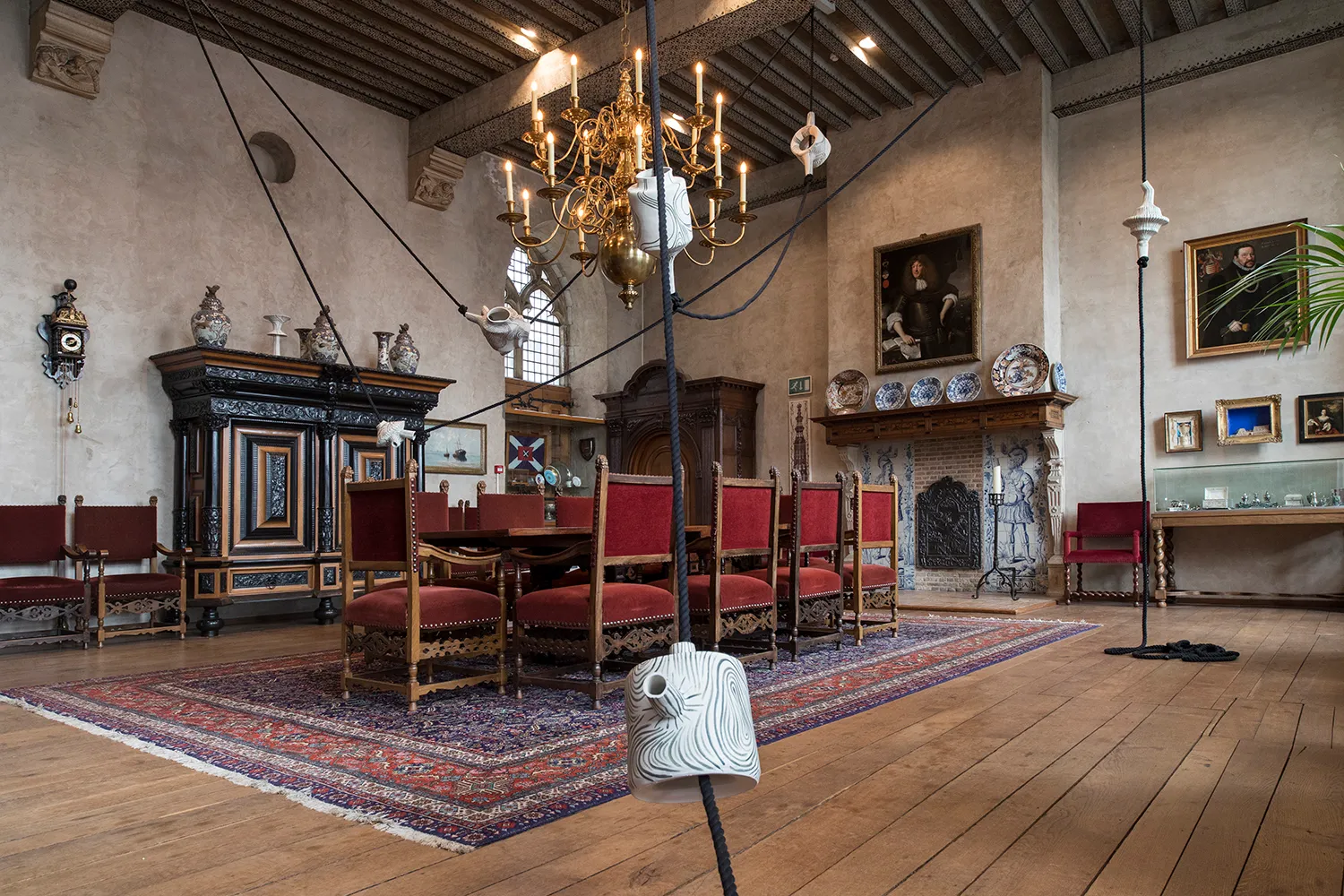 Keramische objecten die op verschillende niveaus aan het plafond hangen, in een zaal met andere schilderijen en antiquiteiten