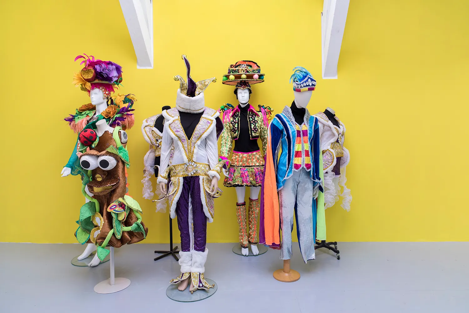7 mannequins met carnavalskostuums staan voor een gele muur