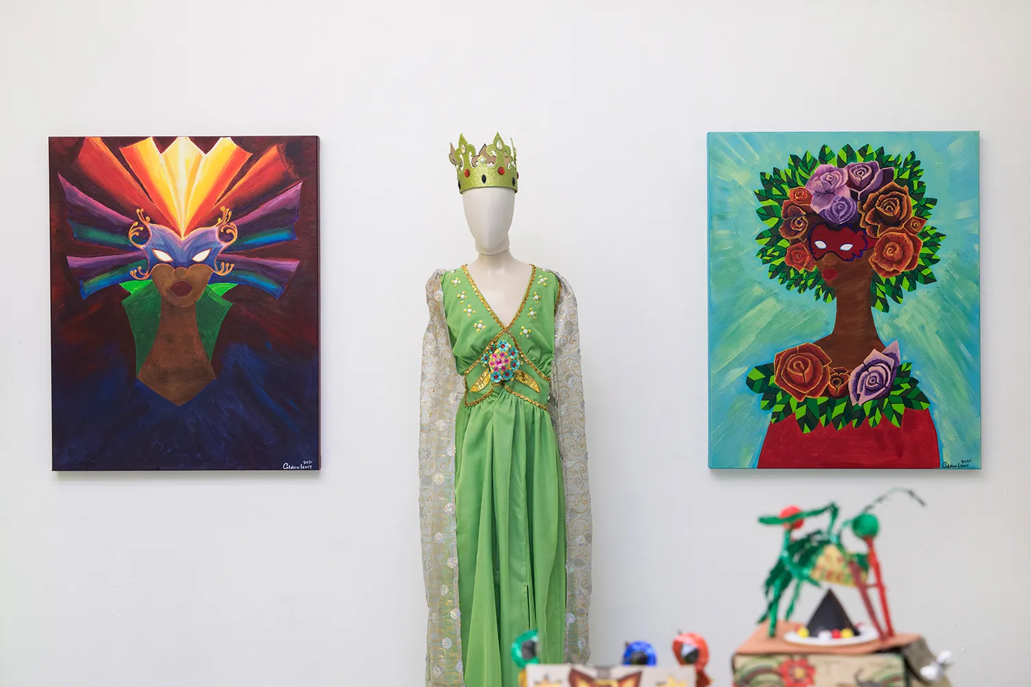 Een gezichtsloze etalagepop met een groene jurk en een kroon staat in het midden van twee schilderijen van een gemaskerde persoon
