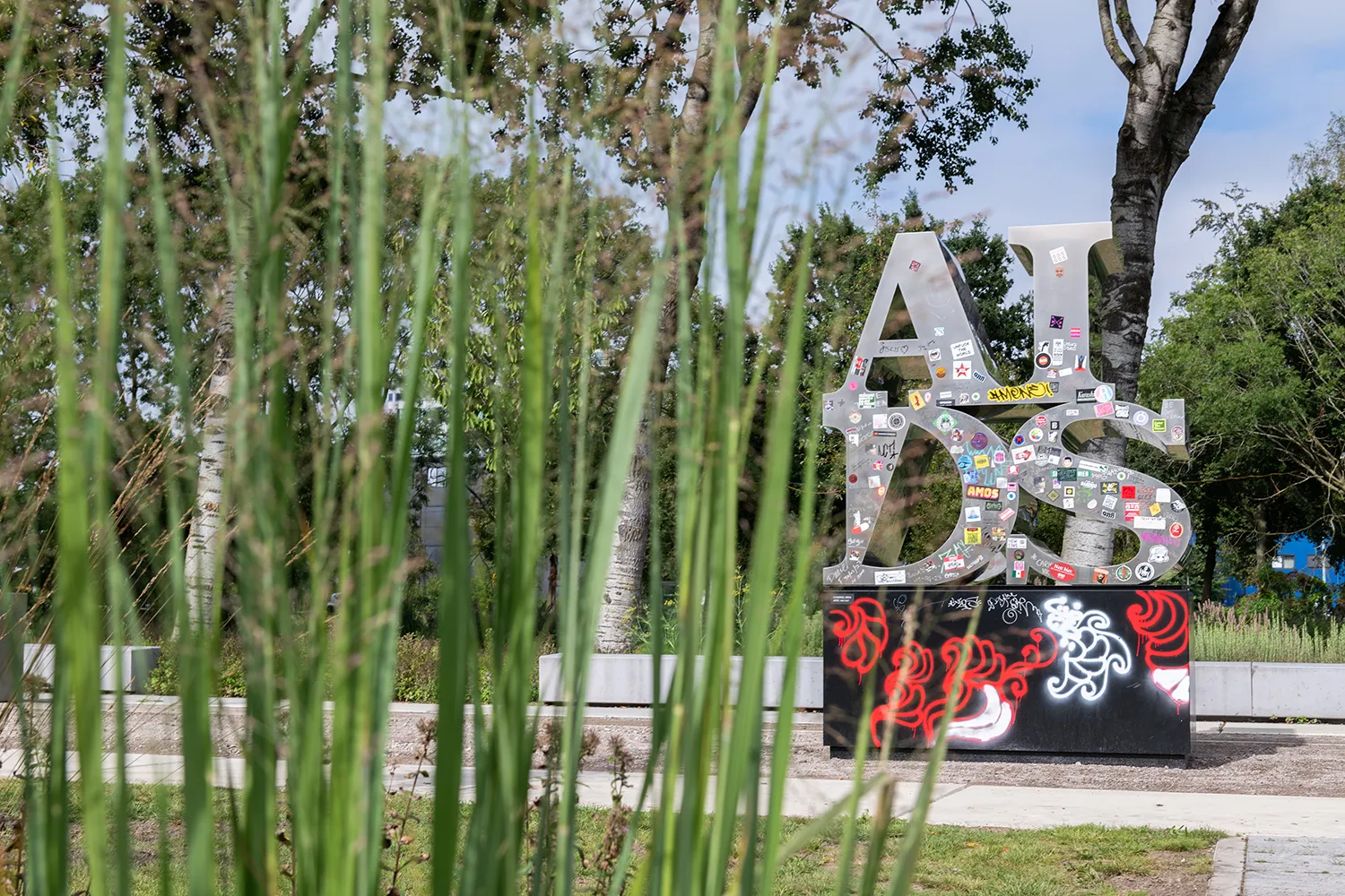 A en I op D en S zilveren metalen letters (leest AIDS) versierd met stickers en andere graffitis geplaatst op een zwarte sokkel in een park